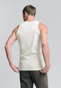 Crèmekleurige mouwloze tanktop van katoen, met een ronde halslijn en een aansluitend ontwerp, gedragen met donkere, loszittende broeken.