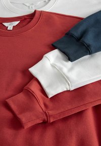 Tres sudaderas apiladas: una sudadera roja con puños de canalé, una sudadera blanca con un acabado suave y una sudadera azul marino con puños texturizados.