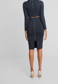 Pruhované přiléhavé šaty v námořnické modři a olivové barvě, s krátkým topem a dlouhými rukávy. Mají zadní zip a rozparek ke kolenům na lemu.