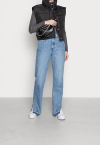 Black puffer vest with high collar, gray sweater underneath, light blue straight-leg jeans, and white sneakers. Small black bag with chain strap.
