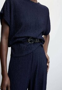 Haut texturé marine à manches courtes, associé à un bas assorti, cintré à la taille par une ceinture noire avec une boucle en métal.