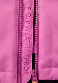 Vaaleanpunainen säänkestävä takki, jossa on kestävä vetoketju ja brodeerattu brändimerkintä. Materiaali näyttää sileältä ja siinä on hienoinen kiilto.