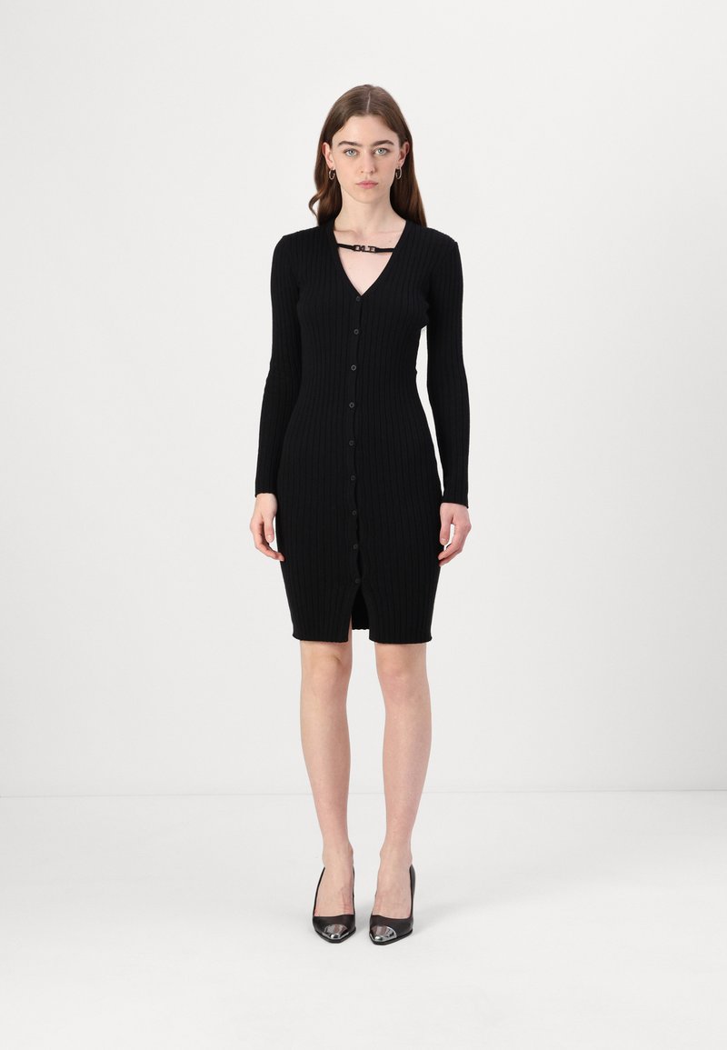 Fekete bordázott kötött ruha hosszú ujjakkal, V-nyakkal, gombos elejével és térd hosszúságú szegéllyel. Egy díszítő pánt részlet található a nyak körül.