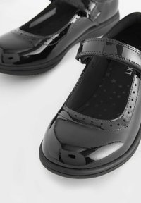 Schwarze, lackierte Mary Jane Schuhe mit runder Zehenpartie, einem einzigen Riemen und durchbrochenen Akzenten am Rand; gemusterte Innensohle.