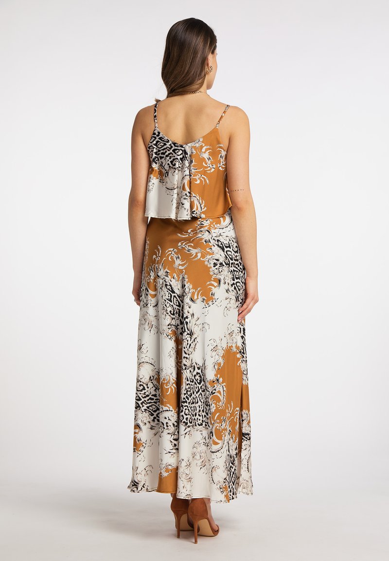 Maxikleid in Orange und Weiß mit floralem und tierischem Muster. Spaghetti-Träger, schichtendes Rückendesign, fließender Stoff, kombiniert mit nackten High Heels.