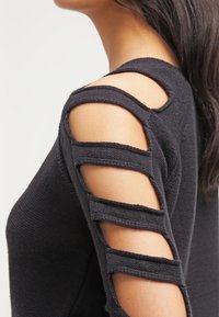 Czarny sweter dzianinowy z wycięciami na ramionach i poziomymi paskami. Szczegółowa tekstura i dopasowany krój podkreślają jego nowoczesny styl.