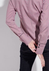 Camicia a quadri rossa e blu con un design aderente e maniche arrotolate, abbinata a jeans in denim scuro. I bottoni decorano i polsini.