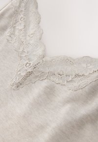 Tissu beige doux avec une bordure délicate en dentelle florale le long d'un décolleté en V, mettant en valeur des motifs et une texture détaillés.