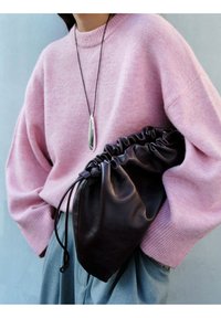 Rosa gestrickter Pullover mit rundem Ausschnitt, kombiniert mit einer schwarzen Lederbeuteltasche mit gerafften Kanten und Kordelzugverschluss.