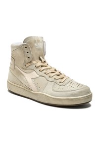 Sneaker alte in suede beige chiaro con puntale perforato, dettagli crema, lacci piatti e suola in gomma testurizzata. Marchio visibile sulla linguetta.