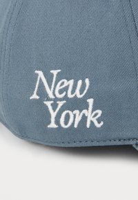 Blå basebollkeps med broderat "New York" i vitt, med en texturerad tyg och böjd skärm. Inga ytterligare detaljer synliga.
