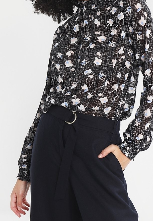 Kwiatowa bluzka w kolorze czarnym z białymi i niebieskimi wzorami, z długimi rękawami i wysokim dekoltem. Połączona z ciemnymi spodniami z wysokim stanem.