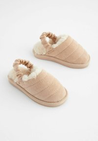Chaussons beiges avec un design en tissu matelassé, doublés de fourrure et dotés d'un talon élastique froncé pour un ajustement parfait. Semelle plate et texturée.
