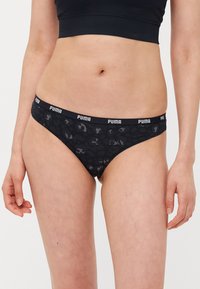 Crno patterned tangice s mekanim elastičnim pojasom koji sadrži bijelo "PUMA" brendiranje. Tkanina ima glatku teksturu i blagi sjaj.