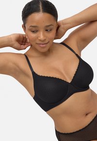 Sujeción negra con encaje en los bordes, presenta un patrón de diamantes texturizado y tirantes ajustables, diseñado para ofrecer comodidad y soporte.