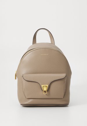 Beige Leder-Rucksack mit abgerundetem Oberteil, goldfarbenen Beschlägen und Frontklappenfach mit Verschluss. Strukturierte Oberfläche und zwei obere Griffe.