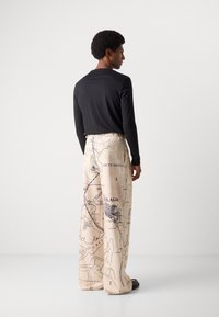 Black long-sleeve shirt paired with beige wide-leg pants featuring a printed map design in black. Smooth fabric with a relaxed fit.
