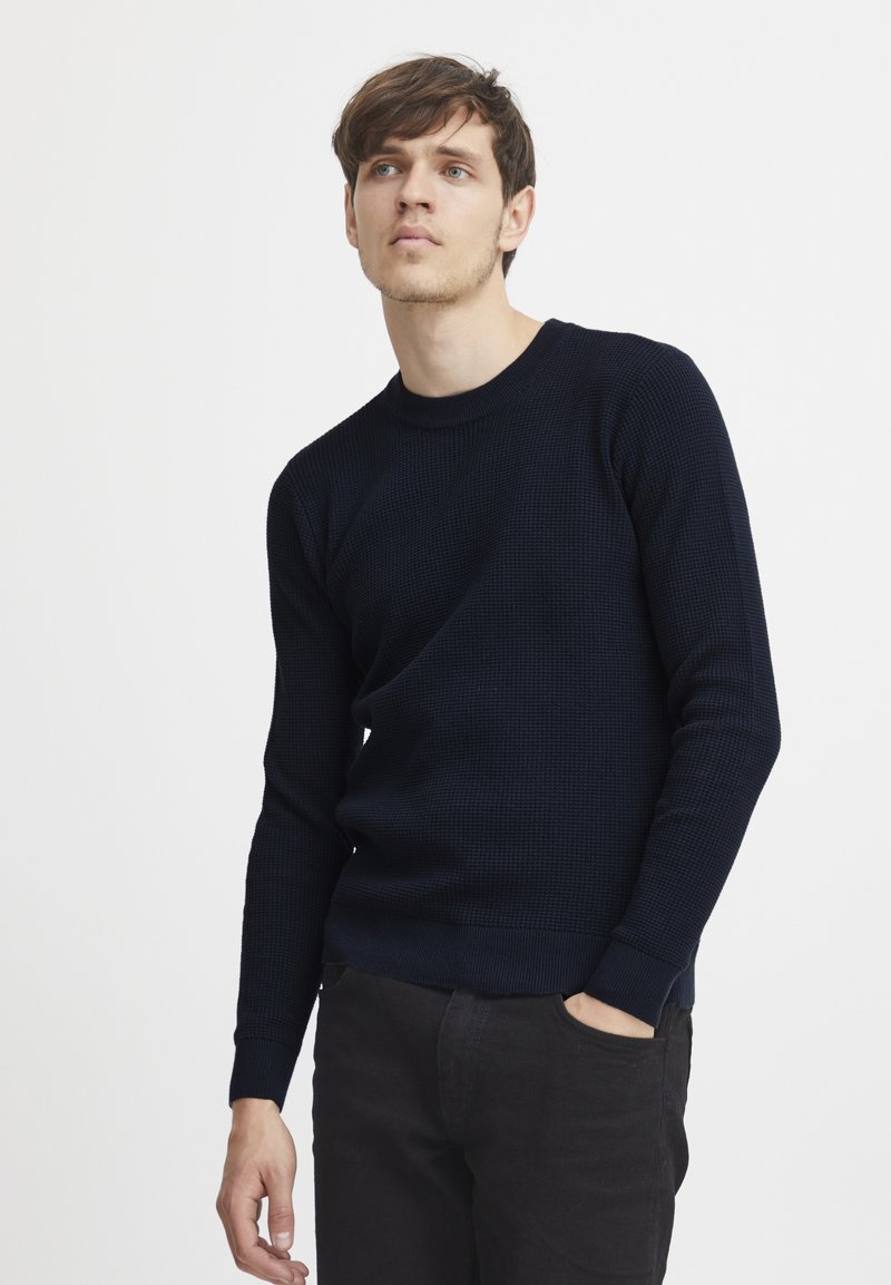 Pulover tricotat bleumarin cu un model texturat, gât rotund și manșete ajustate; asociat cu pantaloni negri.