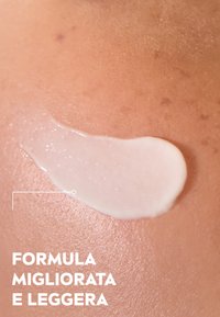Crema bianca applicata su una pelle leggermente strutturata, con una finitura liscia e lucida, su uno sfondo marrone chiaro caldo.