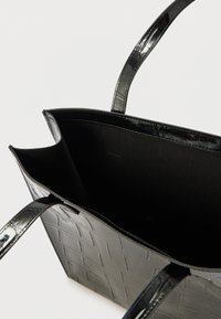 Czarna torba typu tote wykonana z lakierowanej skóry o fakturze krokodyla. Wnętrze wyłożone czarną tkaniną. Posiada podwójne uchwyty do noszenia.