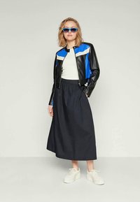 Svart og blå lærjakke med hvite detaljer, kombinert med et høyhånds navy skjørt og hvite joggesko, som skaper et lagdelt utseende.
