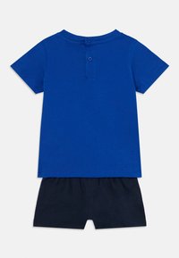 Maglietta in cotone blu con maniche corte e patta con bottoni sul retro, abbinata a pantaloni corti blu navy con cintura elastica.