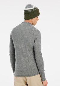 Grijze shirt met lange mouwen en een gestructureerde afwerking, gecombineerd met een groene gebreide beanie met witte en grijze strepen.