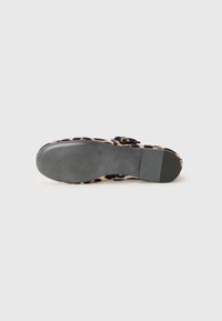Chaussure à motif léopard avec une tige beige texturée, des accents noirs et une semelle en caoutchouc plate. Dispose d'une boucle pour un maintien sécurisé.