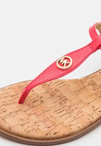 Sandale tongs en cuir rouge avec semelle en liège et logo circulaire MK doré sur la bride sur fond blanc.