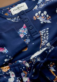 Nočná súprava tmavomodrej farby s kvetinovými vzormi, so zaobleným výstrihom, zapínaním na gombíky a elastickým pásom so šnúrkou.