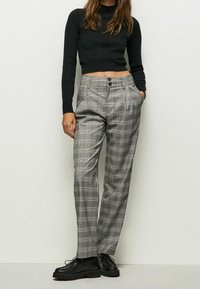 Grå rutiga byxor med lös passform, med framveck, två sidofickor och knäppning. Materialet verkar vara strukturerat.