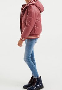 Rosa quiltad pufferjacka med leopardmönstrad foderhuva, elastiska ärmar och randig nederkant, tillsammans med blå skinny jeans och blanka svarta stövlar.