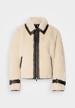 Veste en shearling couleur crème avec des accents en cuir noir, fermeture éclair à l'avant et large col. Comprend des poignets réglables et des poches latérales.