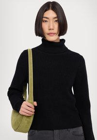 Schwarzer, gerippter Rollkragenpullover kombiniert mit einer grünen Wildleder-Schultertasche, die einen einzelnen Riemen und eine dezente Textur aufweist.