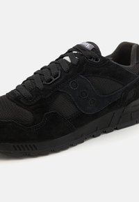 Scarpa sportiva nera realizzata con una combinazione di materiali in suede e mesh. Il design include dettagli texturizzati, un collo imbottito e una suola in gomma con modelli di trazione.