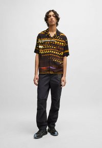 Short-sleeve shirt in dark tones with a light pattern, paired with black cargo pants featuring pockets. Footwear includes black sneakers.