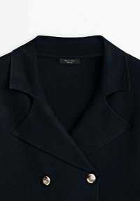 Granatowa marynarka dwuczęściowa z wyłogami, wykonana z miękkiego materiału. Posiada dwa złote ozdobne guziki oraz metkę wewnętrzną.