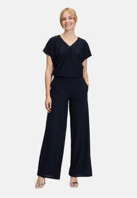 Marineblaues zweiteiliges Outfit mit einem entspannten Schnitt. Das kurzärmelige Oberteil hat einen V-Ausschnitt; die weit geschnittenen Hosen haben seitliche Taschen und einen elastischen Bund.