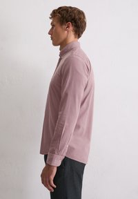 Koszula z długim rękawem w kolorze przybrudzonego różu, wykonana z miękkiej tkaniny. Posiada kołnierzyk zapinany na guziki oraz guziki przy mankietach, dopasowany krój oraz prosty dół.