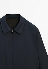 Granatowa kurtka z płaskim kołnierzem i zapięciem na zamek. Wykonana z gładkiego materiału o lekkiej fakturze. Prosty, czysty design bez wzorów.