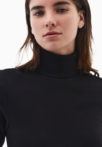 Czarny prążkowany golf o dopasowanym kroju, z wysokim kołnierzem i długimi rękawami. Tkanina jest gładka i lekko elastyczna.