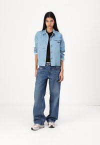 Lys blå denimjakke med knapper foran, brystlomme og en avslappet passform, kombinert med løstsittende blå jeans og rosa sneakers.