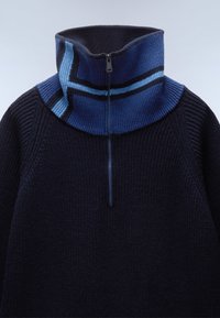 Gebreid sweater met een hoge kraag in donker marineblauw, met een ritsluiting en lichtblauwe gestreepte accenten bij de hals. Geverfd textuurafwerking.