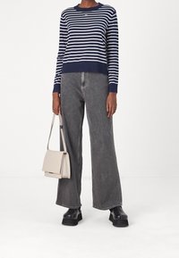 Granatowy i biały sweter w paski z okrągłym dekoltem, zestawiony z szarymi, szerokimi jeansami o wysokim stanie. Niesie beżową torebkę na ramię. Czarne buty na platformie.
