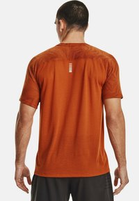 Oranžové sportovní tričko s krátkým rukávem, vzorovanou texturou a ventilačními detaily. Na zádech má obdélníkový akcent.