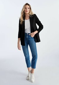 Czarna marynarka na białej bluzce, zestawiona z niebieskimi spodniami typu tapered i białymi trampkami. Gładkie materiały i dopasowany krój.