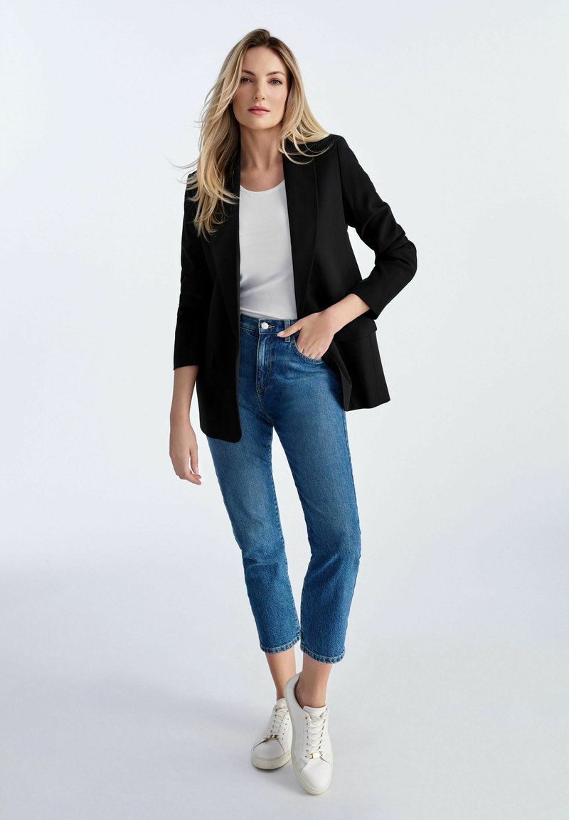 Czarna marynarka na białej bluzce, zestawiona z niebieskimi spodniami typu tapered i białymi trampkami. Gładkie materiały i dopasowany krój.