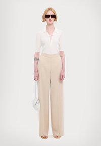 Top bianco a costine con dettagli alla scollatura, pantaloni beige a vita alta e gamba larga, occhiali da sole neri e una piccola borsa intrecciata bianca.