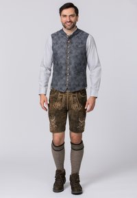 Traditionelles bayerisches Outfit mit einer grauen, strukturierten Weste, braunen Lederhosen mit floralen Stickereien, knielangen Strümpfen und Stiefeln.