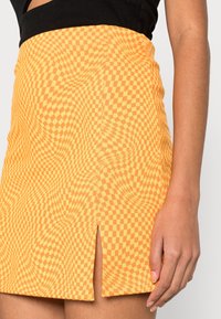 Gonna corta a scacchi arancione con un sottile motivo a spirale e uno spacco frontale, realizzata in un tessuto elastico per una silhouette aderente.